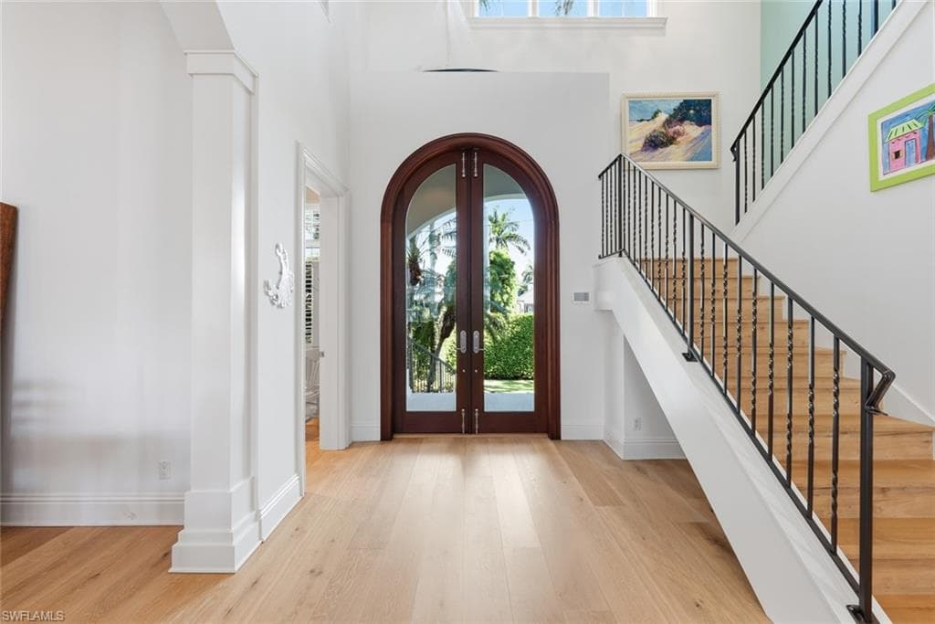 Arch-top French doors with clear glass panels, wood-finish flooring, white painted walls, and a staircase with wrought iron balusters