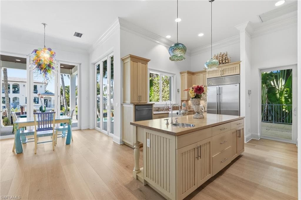 Spacious kitchen featuring light wood-finish flooring, a central island with an integrated sink, built-in stainless steel appliances, and extensive cabinetry