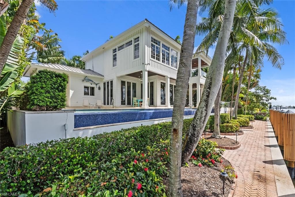 Multi-story coastal residence featuring a second-level balcony, ground-level patio access, and a waterside infinity-edge pool