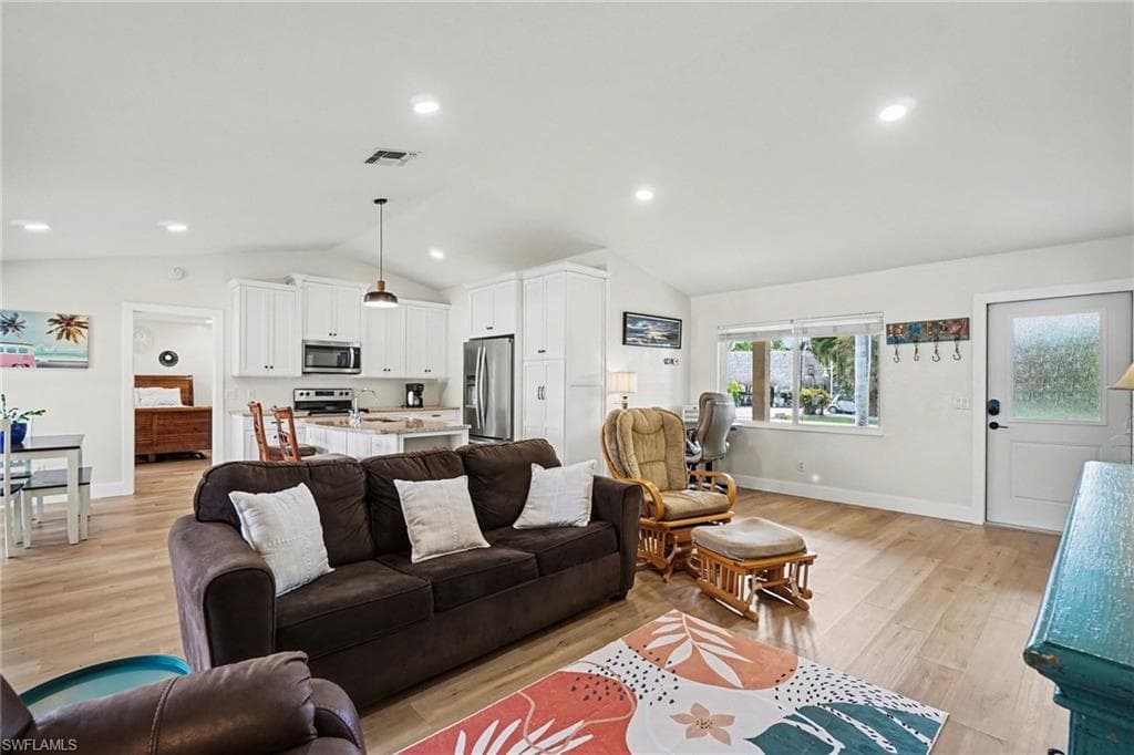 Vaulted ceilings, wood-finish flooring, recessed lighting, white cabinetry, and stainless steel appliances