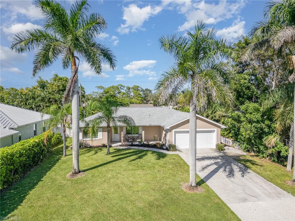 Single-story residence with a two-car garage, concrete driveway, and mature palm trees
