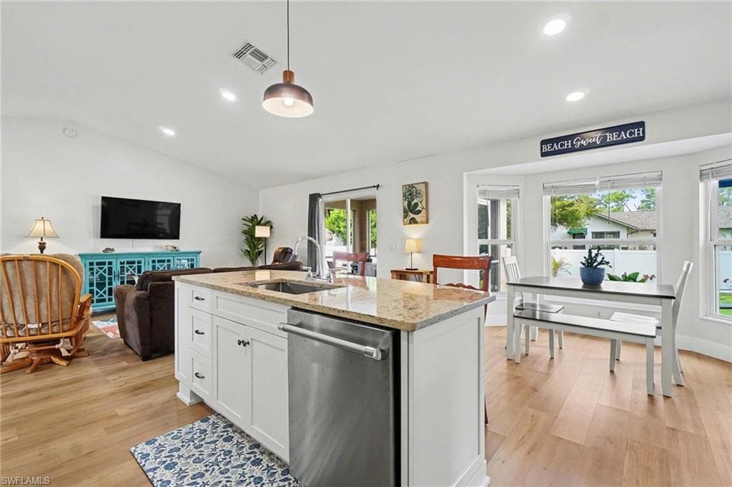 Open-concept living area with wood-finish flooring, white cabinetry, a kitchen island with a built-in sink, and a bay window