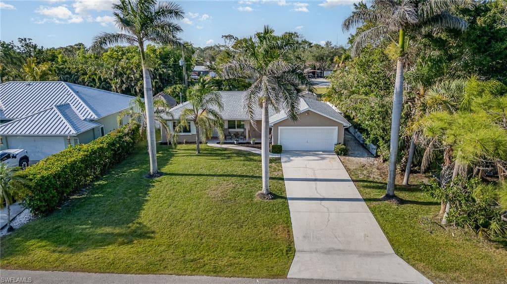 Well-maintained lawn, mature palm trees, concrete driveway, attached garage, and stucco exterior