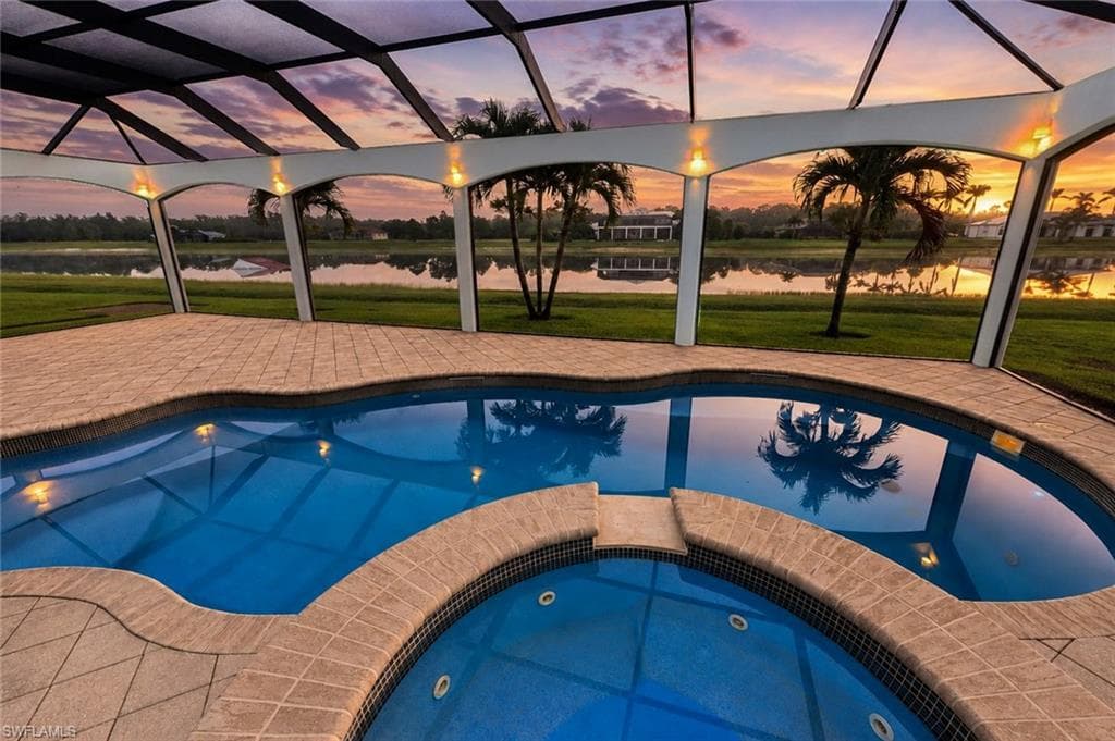 Resort-style outdoor living space featuring a zero-entry saltwater pool with integrated spa, surrounded by travertine decking and enclosed within a glass-paneled lanai structure