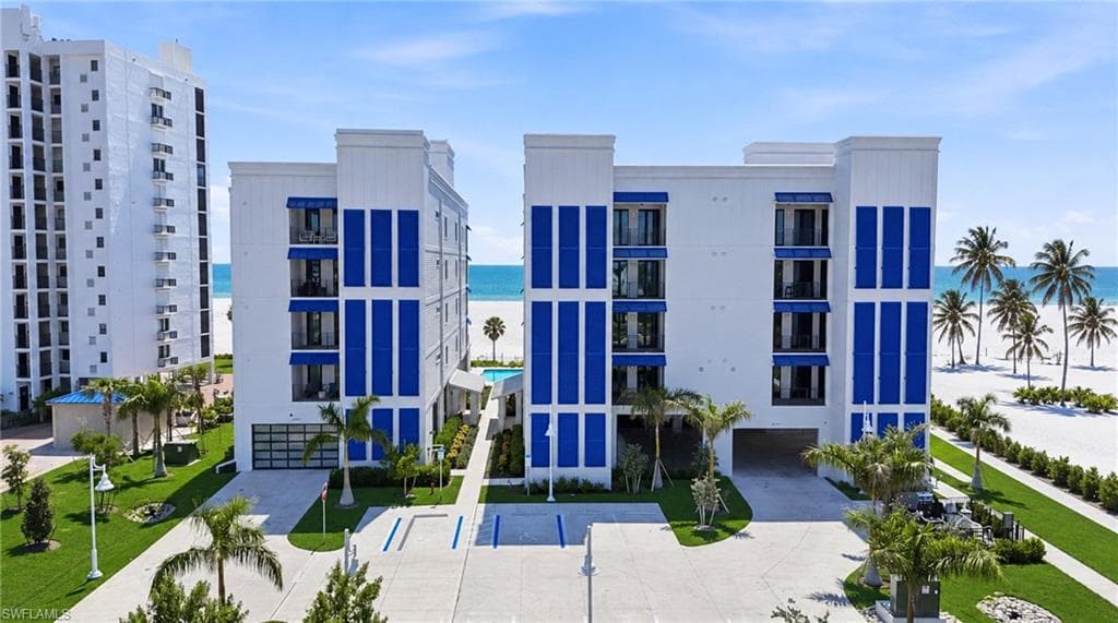 Modern stucco exterior with prominent blue accents, multiple balconies, a covered parking area, and mature palm trees - Virtually Edited Image