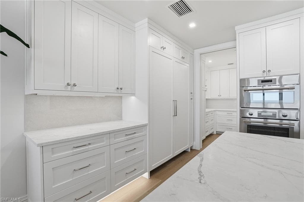 Kitchen with light stone countertops, white cabinets, stainless steel double oven, dark wood finished floors, and recessed lighting