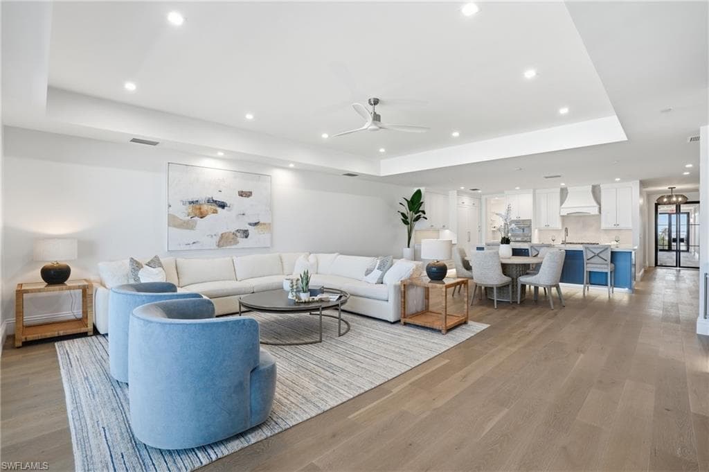 Living room featuring a tray ceiling, light wood-style flooring, a ceiling fan, and recessed lighting