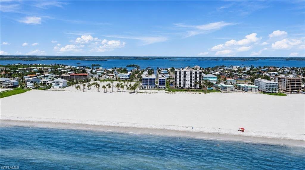 Expansive white sand beach with clear blue water and distant waterfront properties - Virtually Edited Image