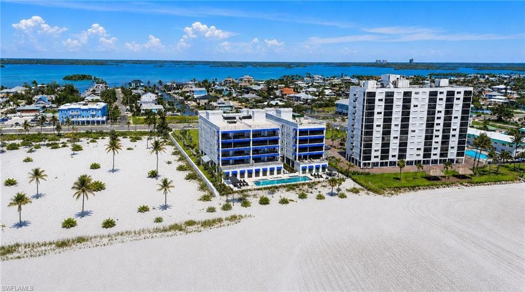 Coastal proximity, expansive white sand beach, multiple multi-story buildings, and direct water access - Virtually Edited Image