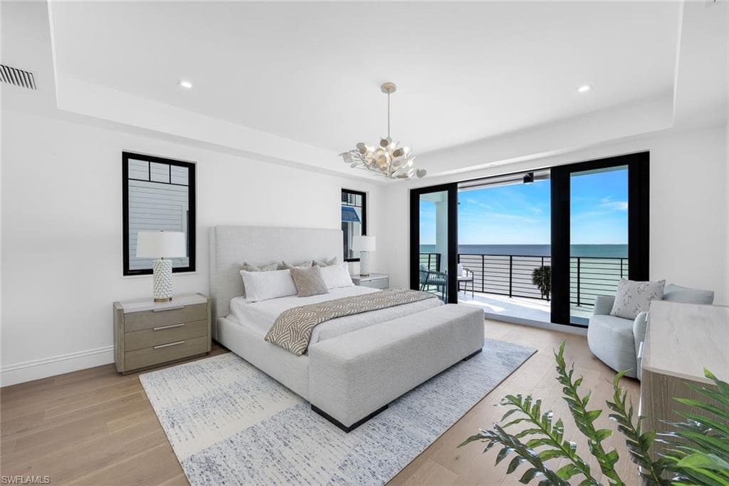 Bedroom with a water view, a raised ceiling, light wood-style flooring, access to exterior, and suspended lighting