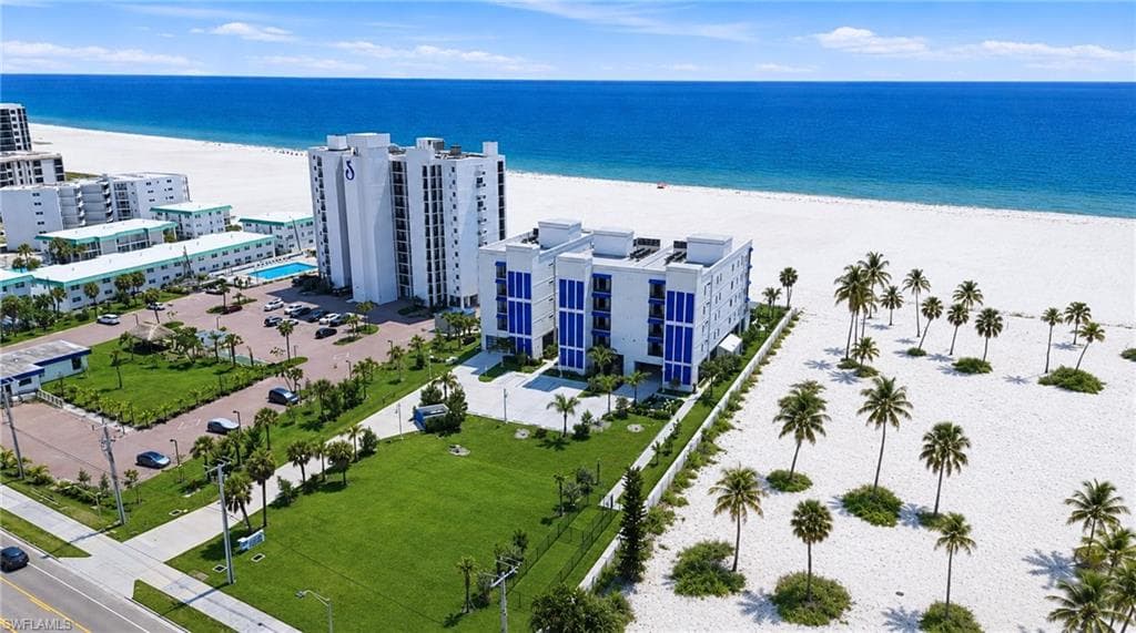 Coastal property featuring a white sand beach, expansive blue ocean, and mature palm treesExpansive land parcel with direct beach access, surrounded by established buildings and roadways - Virtually Edited Image