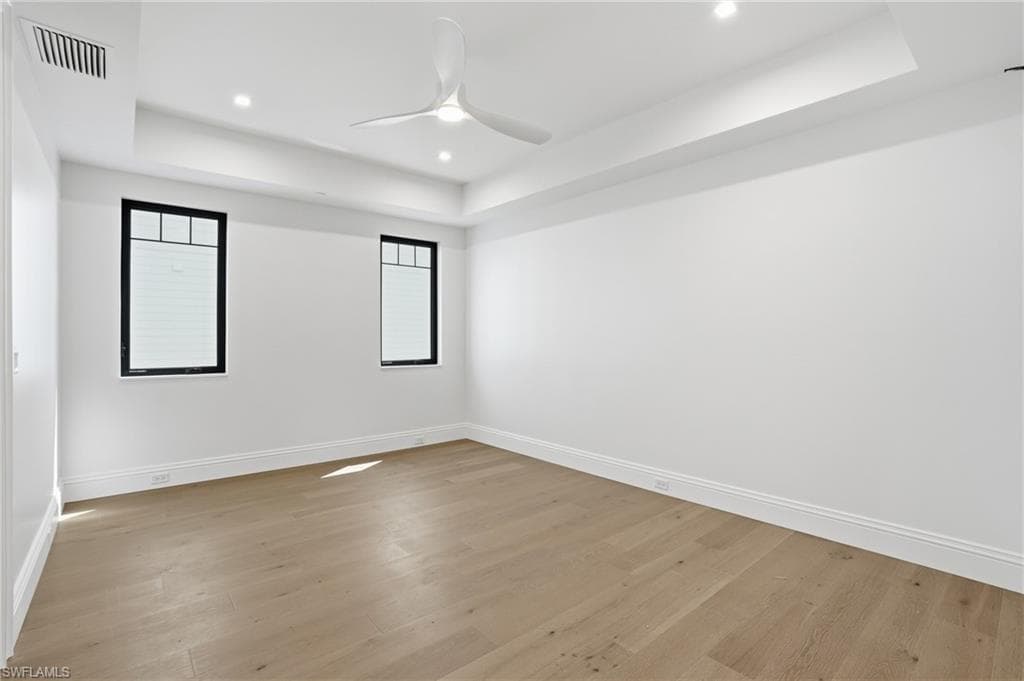 Empty room featuring a raised ceiling, ceiling fan, light wood finished floors, and recessed lighting
