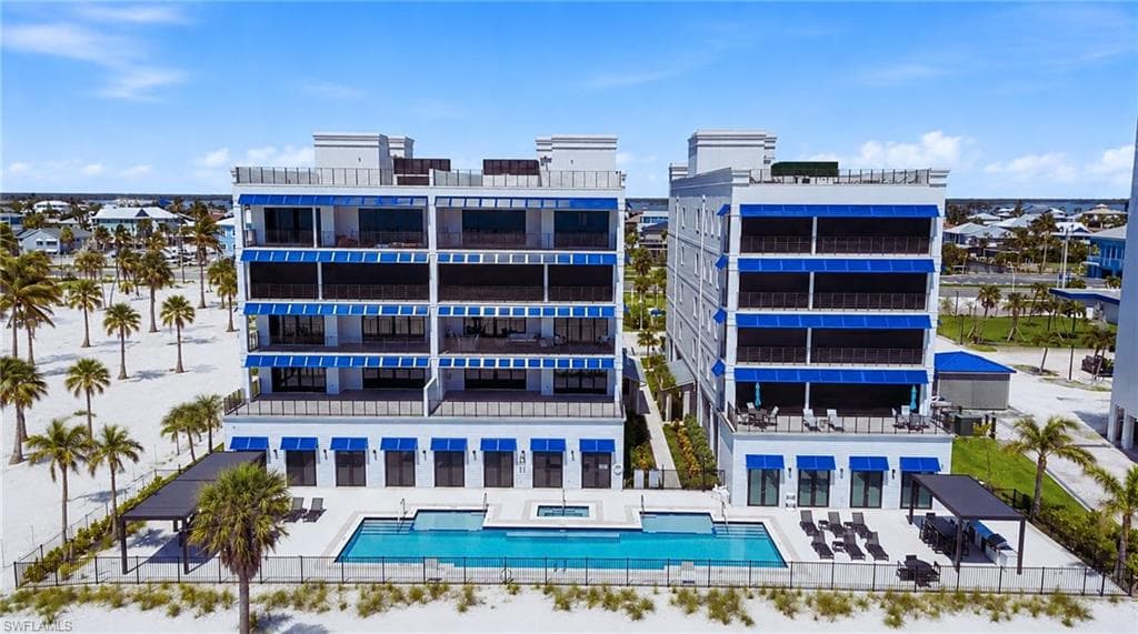 Multi-story building featuring private balconies with awnings, ground-level awnings, and a concrete pool deck with a rectangular pool and integrated spa - Virtually Edited Image
