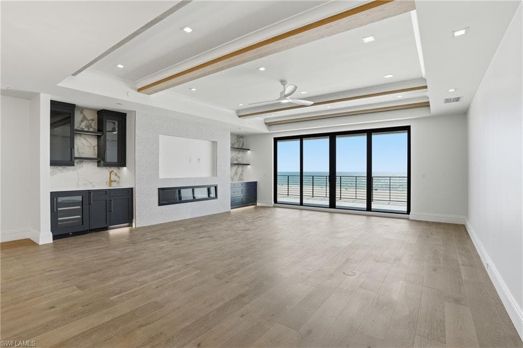 Unfurnished living room featuring light wood-type flooring, a ceiling fan, beamed ceiling, recessed lighting, and a tray ceiling