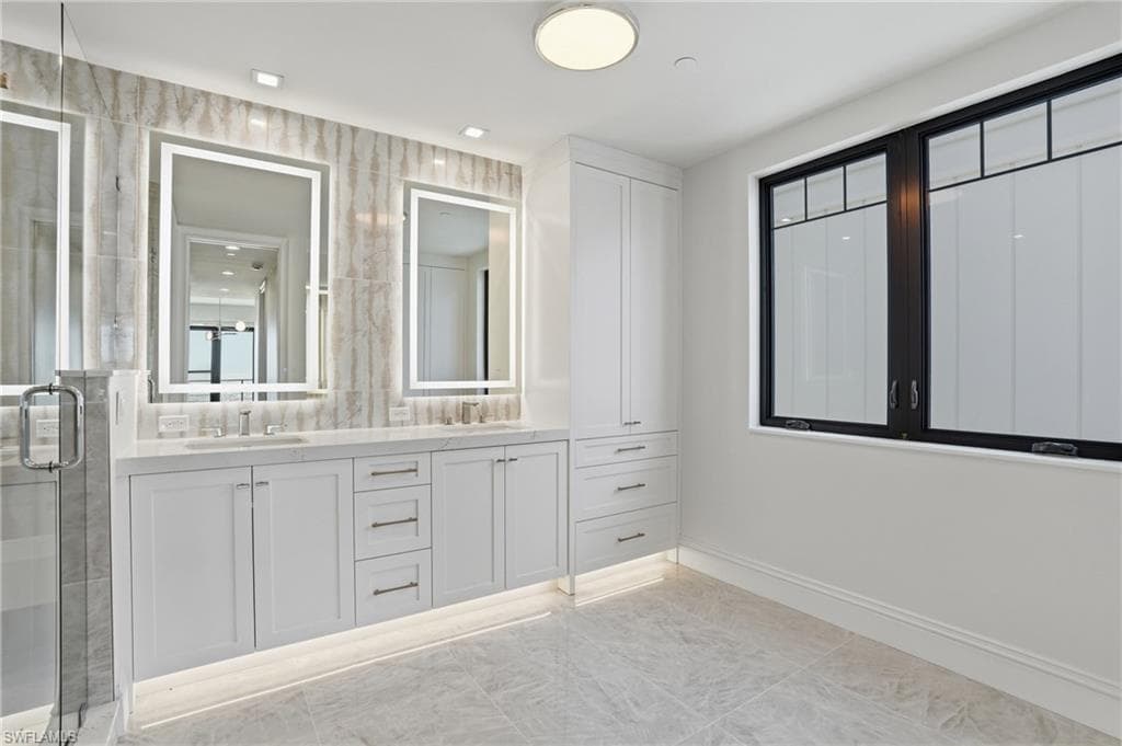 Full bath featuring double vanity, a shower stall, and light marble finish flooring