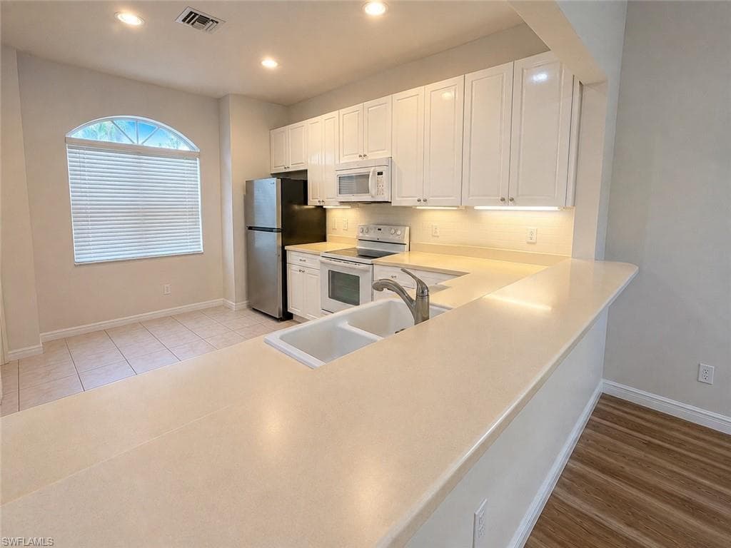 Kitchen featuring white cabinetry, stainless steel appliances, a dual-basin sink, and a breakfast bar