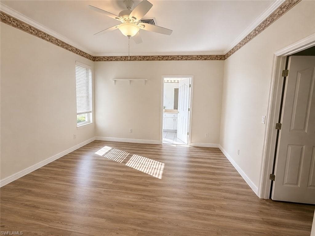 Wood-finish flooring, ceiling fan with integrated lighting, window with blinds, crown molding, and white interior doors
