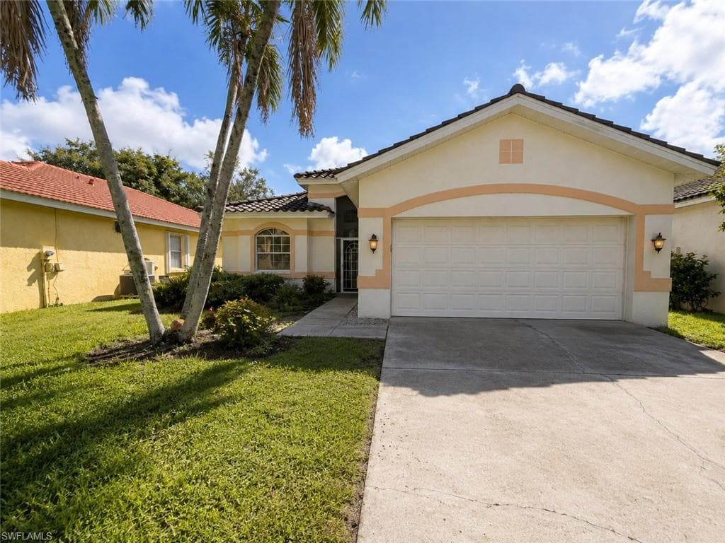 Stucco exterior with a tiled roof, featuring a two-car garage, concrete driveway, and front landscaping