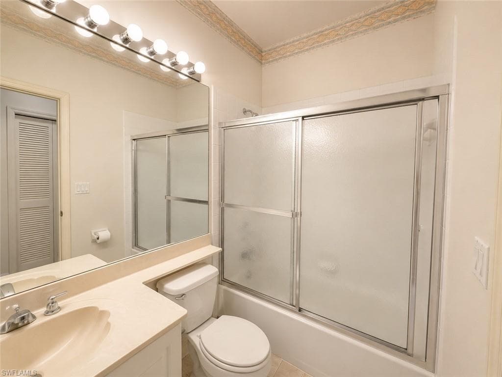 Bathroom with a single vanity, integrated sink, mirrored wall, and a bathtub with sliding frosted glass doors