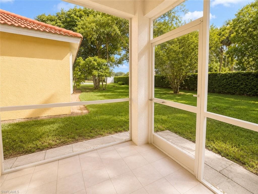 Bright sunroom with expansive glass panels framing manicured grounds, mature landscaping, and lush green lawn