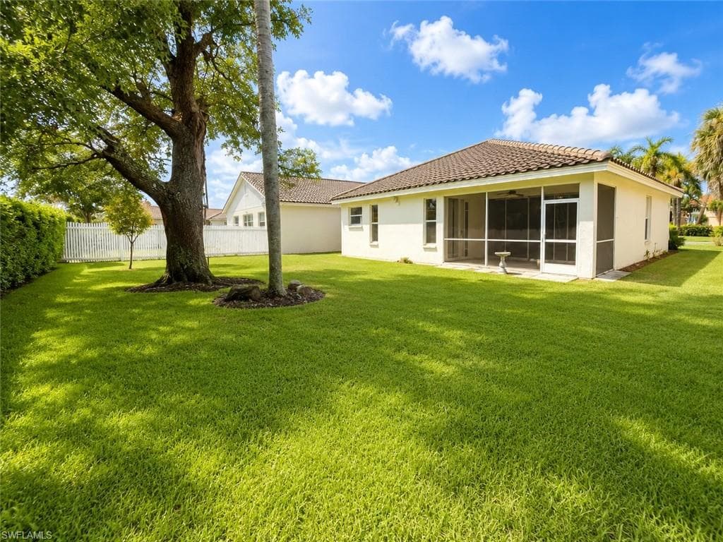 Expansive backyard featuring a manicured lawn, mature trees, and a screened patio