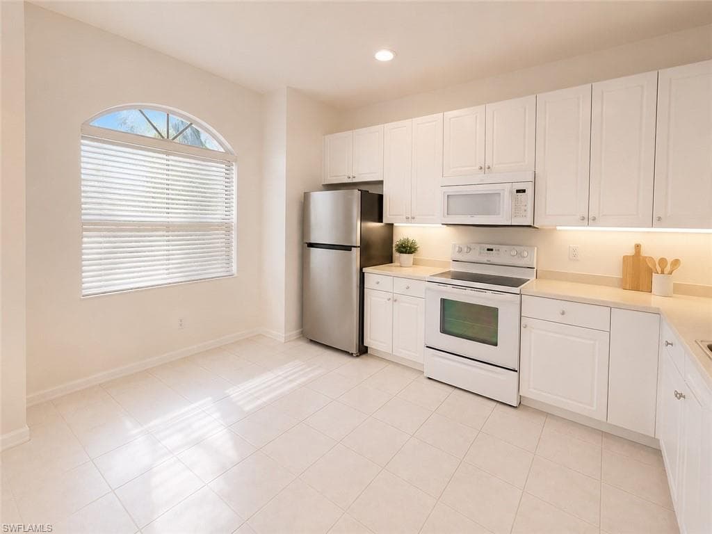 Kitchen with white cabinetry, stainless steel refrigerator, white electric range, white microwave, and light-toned countertops