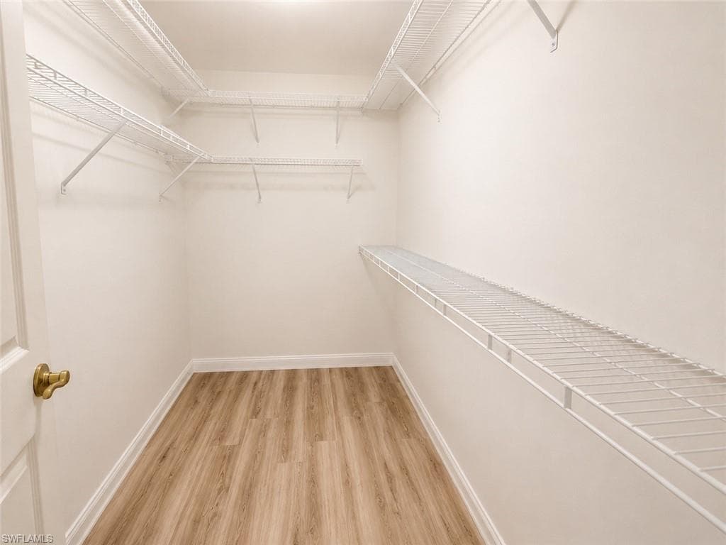 Walk-in closet with multiple white wire shelving units and wood-finish flooring