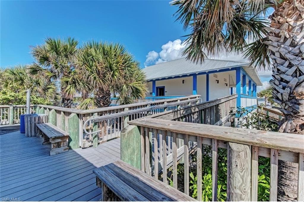 Elevated boardwalk with integrated benches, mature palm trees, and a building featuring blue accents and a metal roof