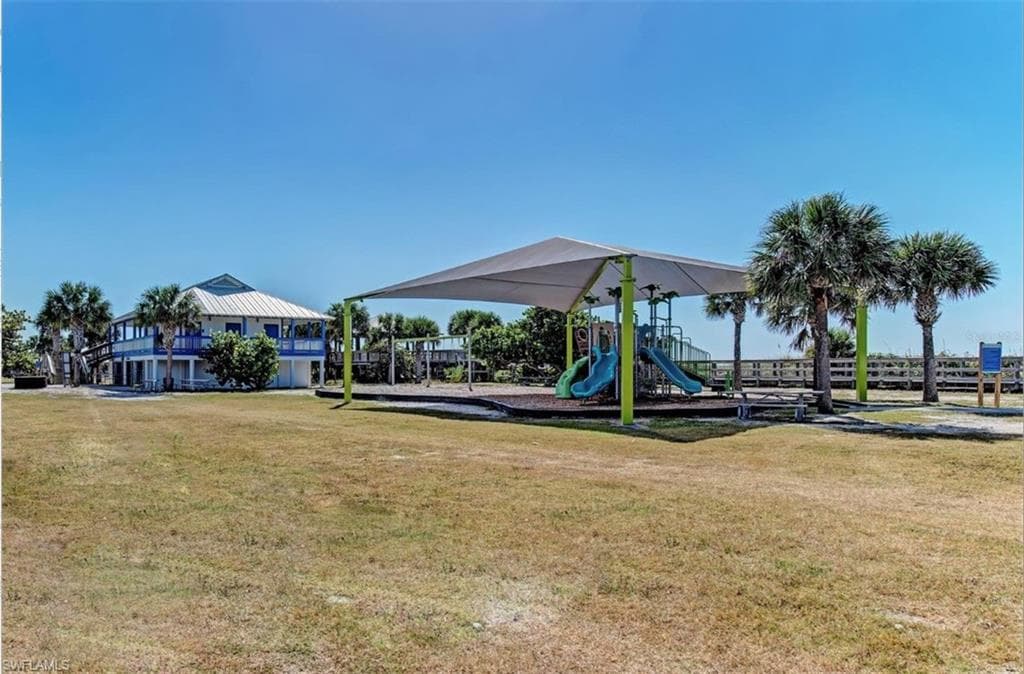 Expansive green space featuring a shaded playground with multiple slides, and a nearby two-story structure with wrap-around balconies