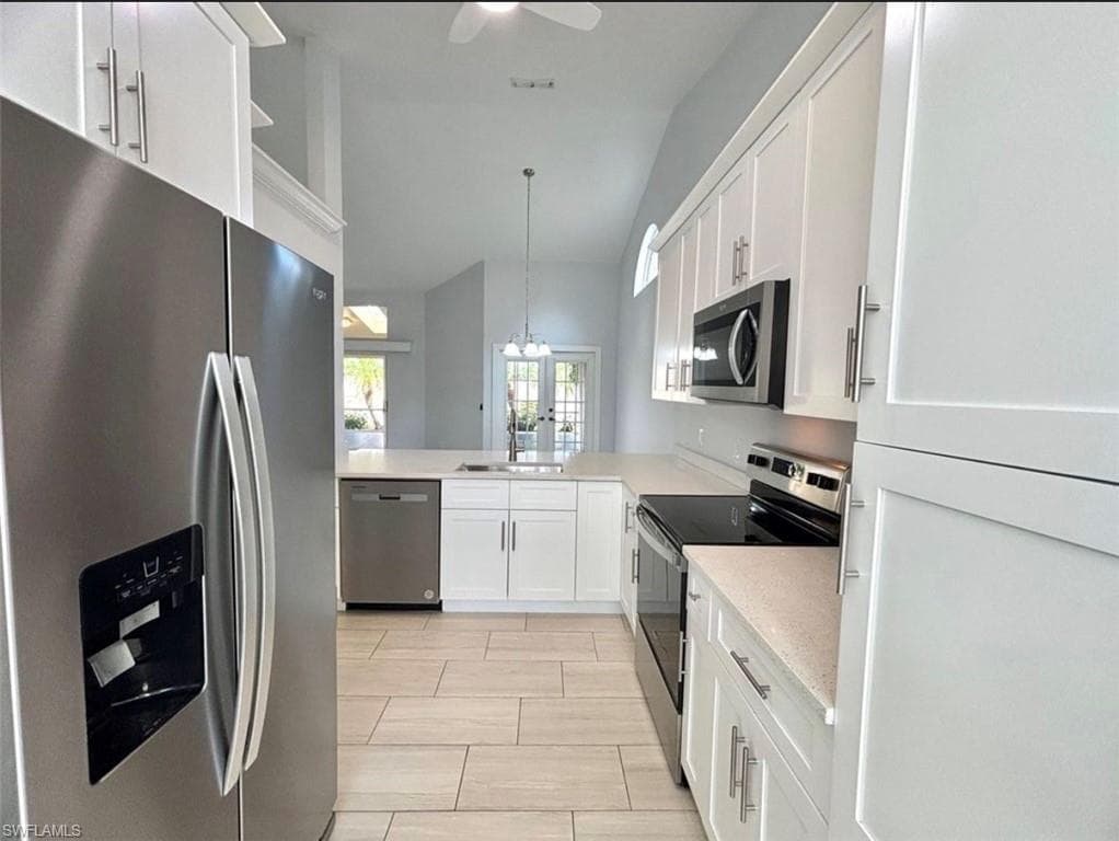 Kitchen featuring stainless steel appliances, white cabinets, lofted ceiling, light stone counters, and a ceiling fan