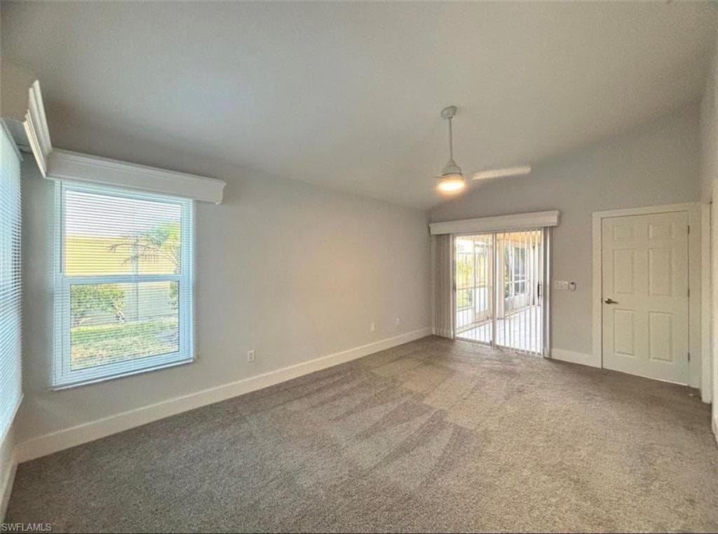 Carpeted spare room featuring baseboards and vaulted ceiling