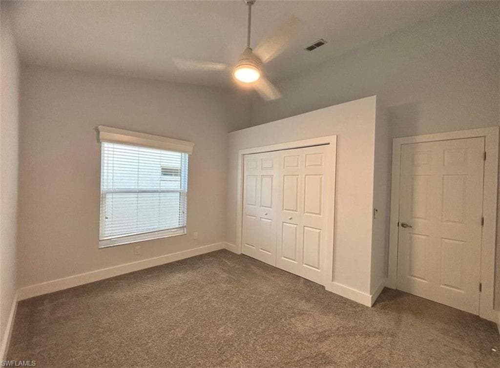 Unfurnished bedroom featuring dark colored carpet, a closet, and ceiling fan