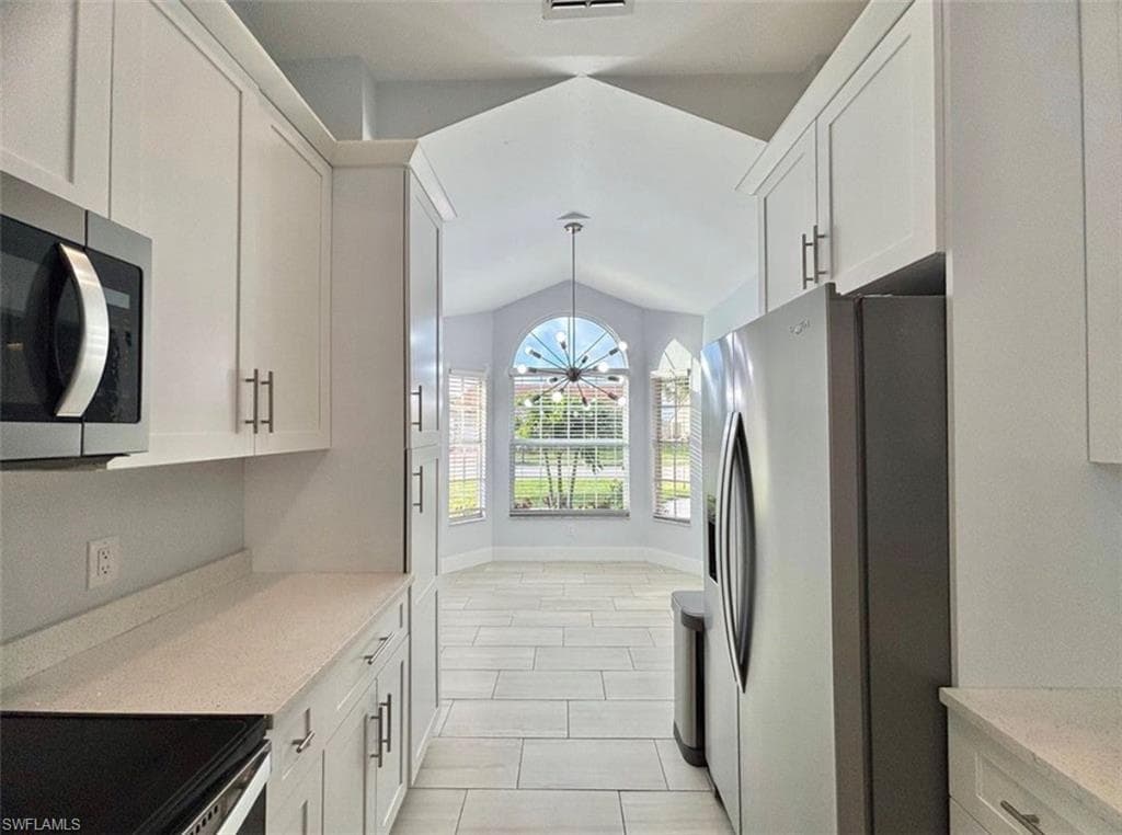 Kitchen featuring stainless steel appliances, white cabinetry, hanging lights, vaulted ceiling, and light stone counters