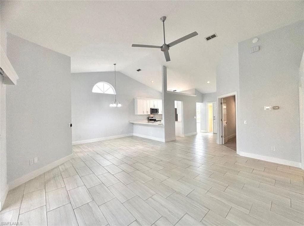 Unfurnished living room with vaulted ceiling, ceiling fan, a chandelier, and wood tiled floors