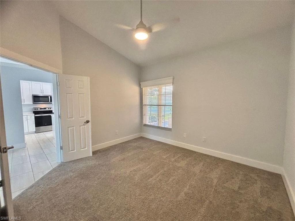 Spare room featuring light carpet, lofted ceiling, ceiling fan, and light tile patterned flooring