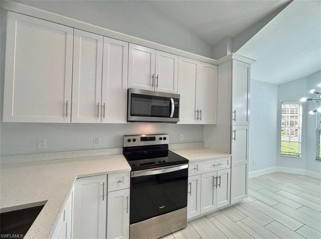 Kitchen with lofted ceiling, stainless steel appliances, white cabinets, light stone countertops, and wood tiled floors