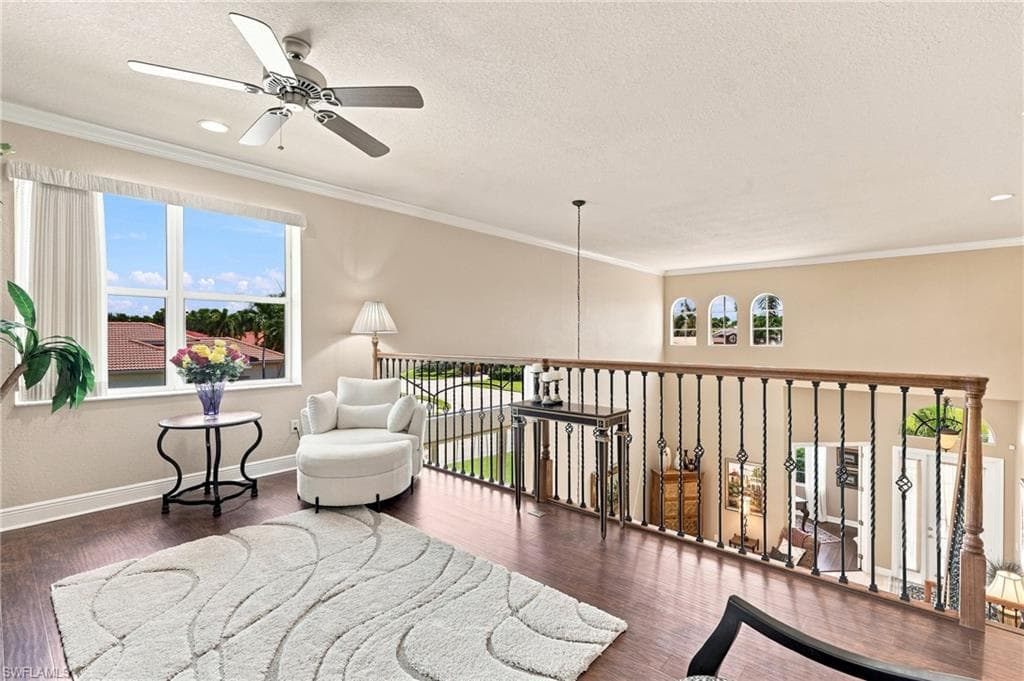 Upper-level landing featuring wood-finish flooring, a ceiling fan, and decorative wrought iron railing