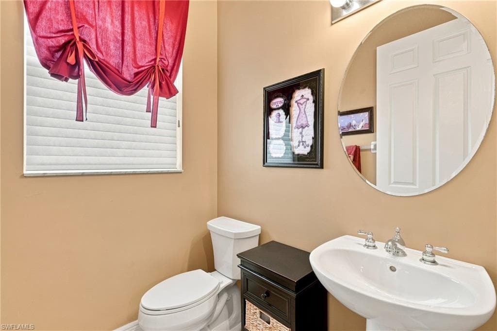 Pedestal sink with chrome fixtures, oval mirror, and a window with blinds