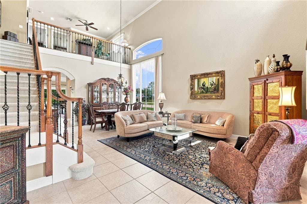 Two-story living area featuring high ceilings, a grand staircase with wrought iron balusters, tile flooring, and large windows with arched transoms