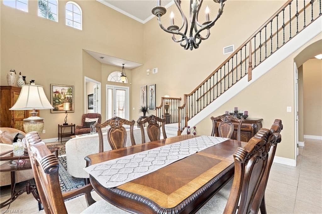 Vaulted ceiling with decorative chandelier, arched windows, grand staircase with wrought iron balusters, wood-finish flooring, and double French doors