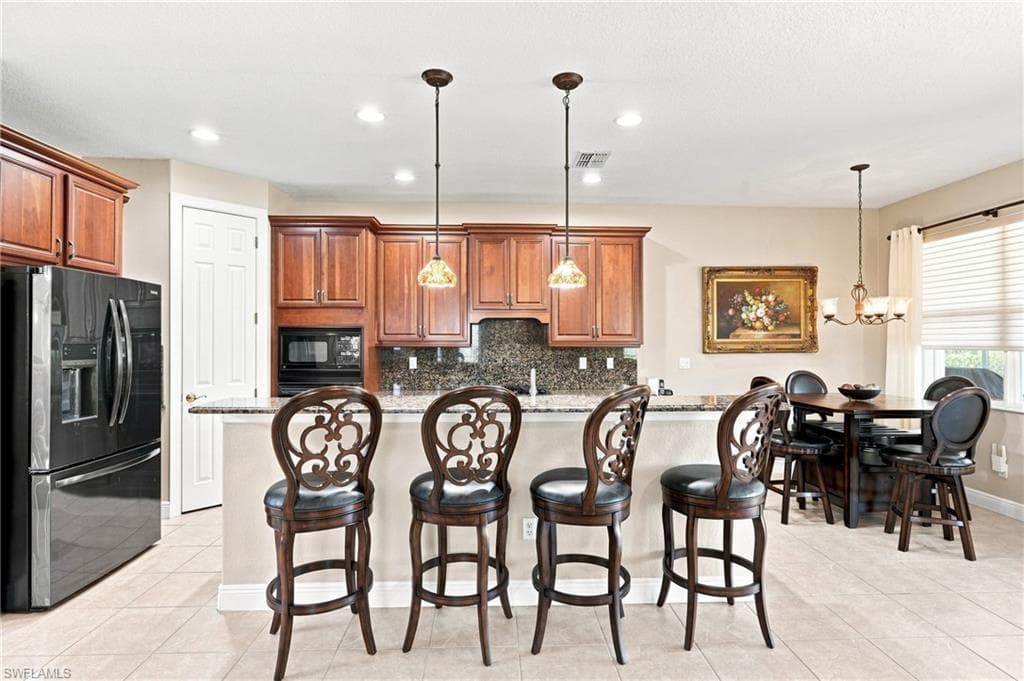Kitchen featuring wood cabinetry, integrated microwave, pendant lighting, and a breakfast bar with stone countertops
