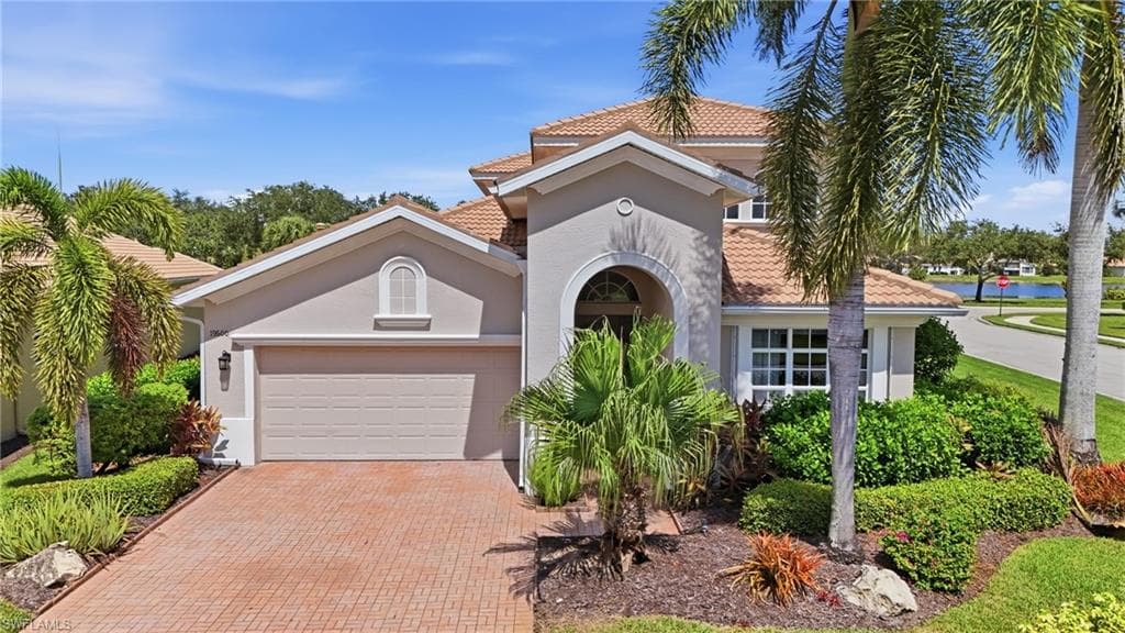 Stucco exterior with a tile roof, arched entry, paver driveway, and an integrated garage