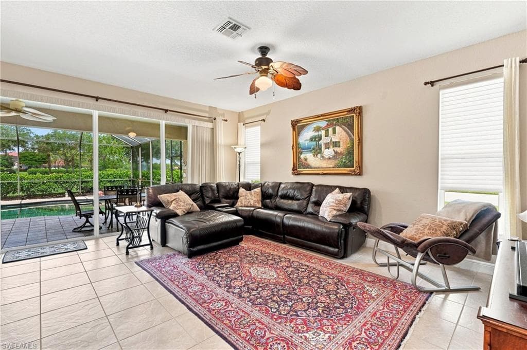 Spacious living area featuring tile flooring, ceiling fan, and large windows with privacy blinds