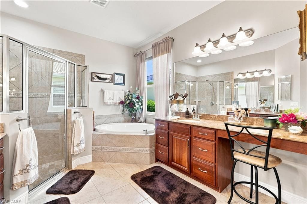 Walk-in shower with clear glass enclosure, built-in soaking tub, wood-finish vanity with ample storage, large vanity mirror, and tile flooring