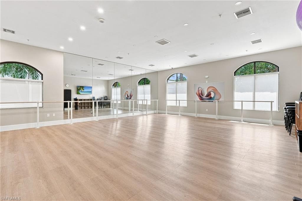 Spacious room featuring wood-finish flooring, full-wall mirrors, integrated ballet barres, recessed lighting, and arched windows with roller shades