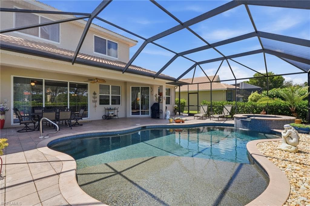 Screened-in pool deck featuring a freeform swimming pool, integrated spa with waterfall, and a tiled patio