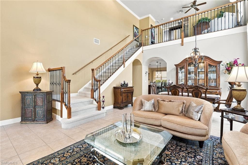 Two-story living area with high ceilings, tile flooring, and a grand staircase with wood newel posts and wrought iron balusters