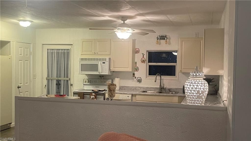 Kitchen with sink, white appliances, and ceiling fann