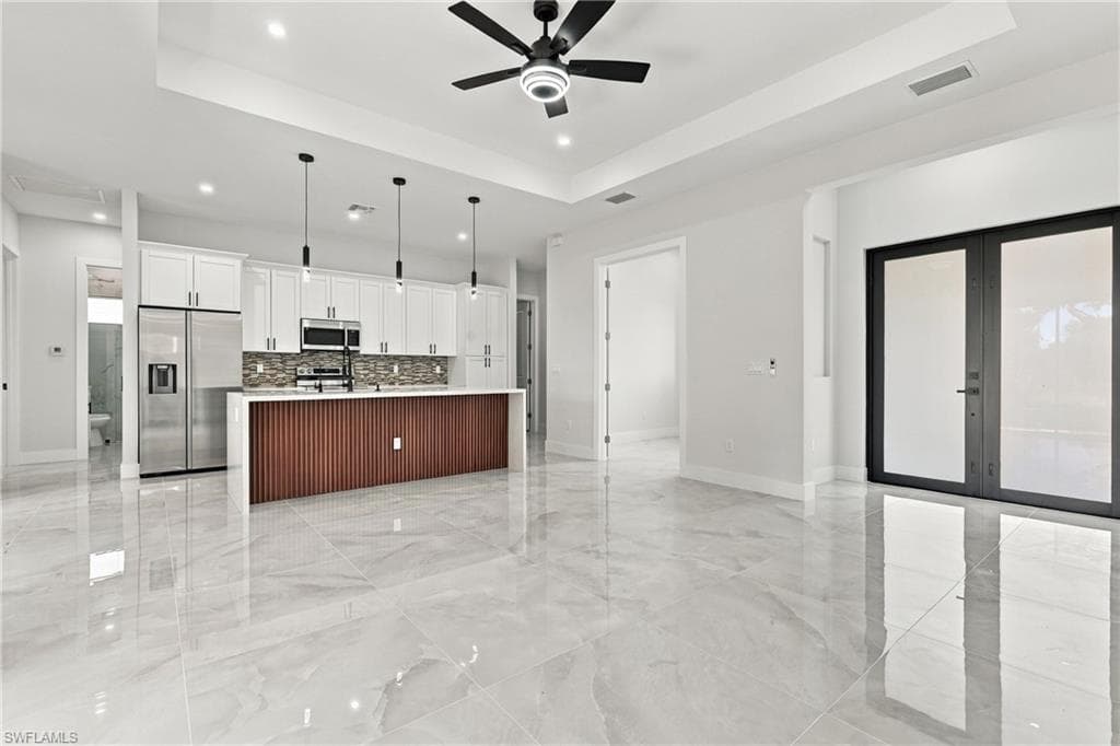 White kitchen cabinetry, stainless steel appliances, a center island with a wood-finish accent, pendant lighting, and polished floor tiling