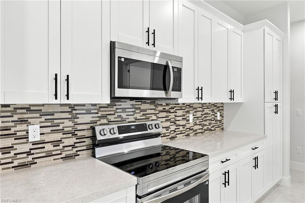 White shaker-style cabinetry, quartz countertops, stainless steel appliances, and a mosaic tile backsplash